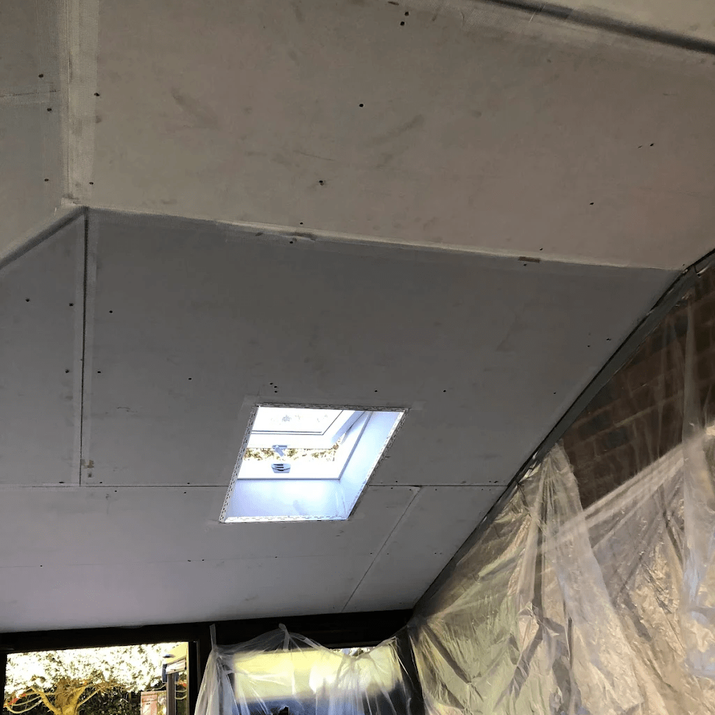 Plasterboard ceiling with a skylight and exposed brick wall.