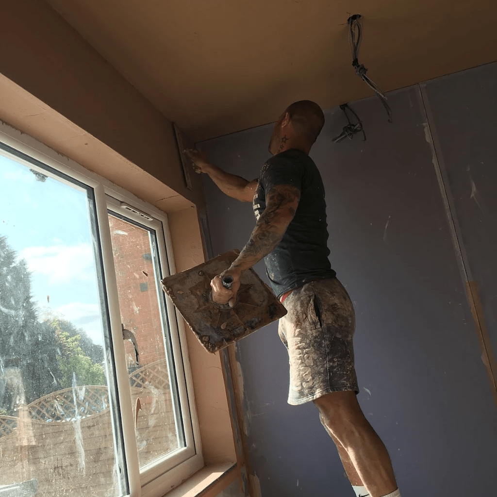Plasterer applying plaster to an interior wall using a trowel.