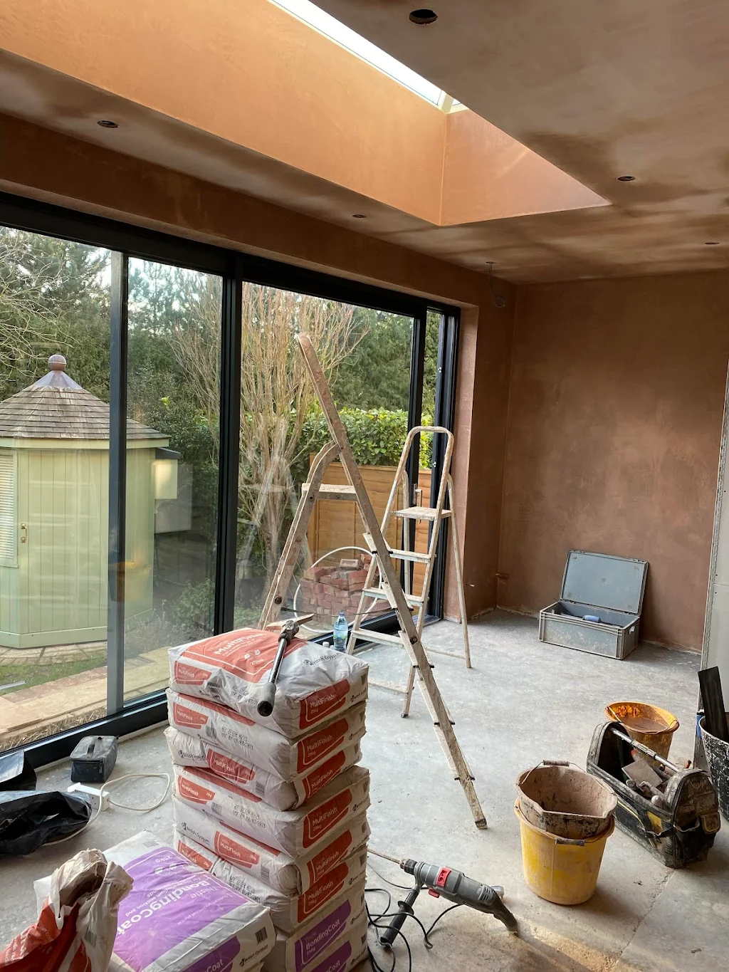 Interior plastering project with plastering materials, tools and ladders in a partially finished room