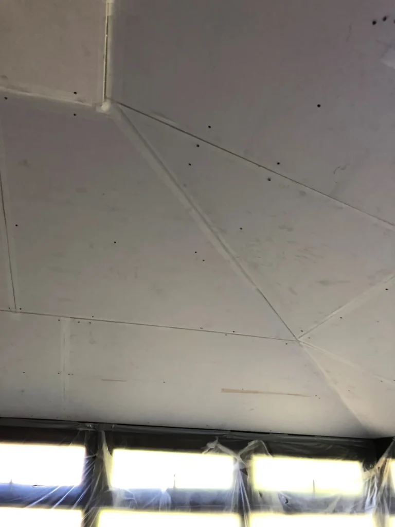 Plasterboard ceiling installation with visible joints and screw fixings above covered windows