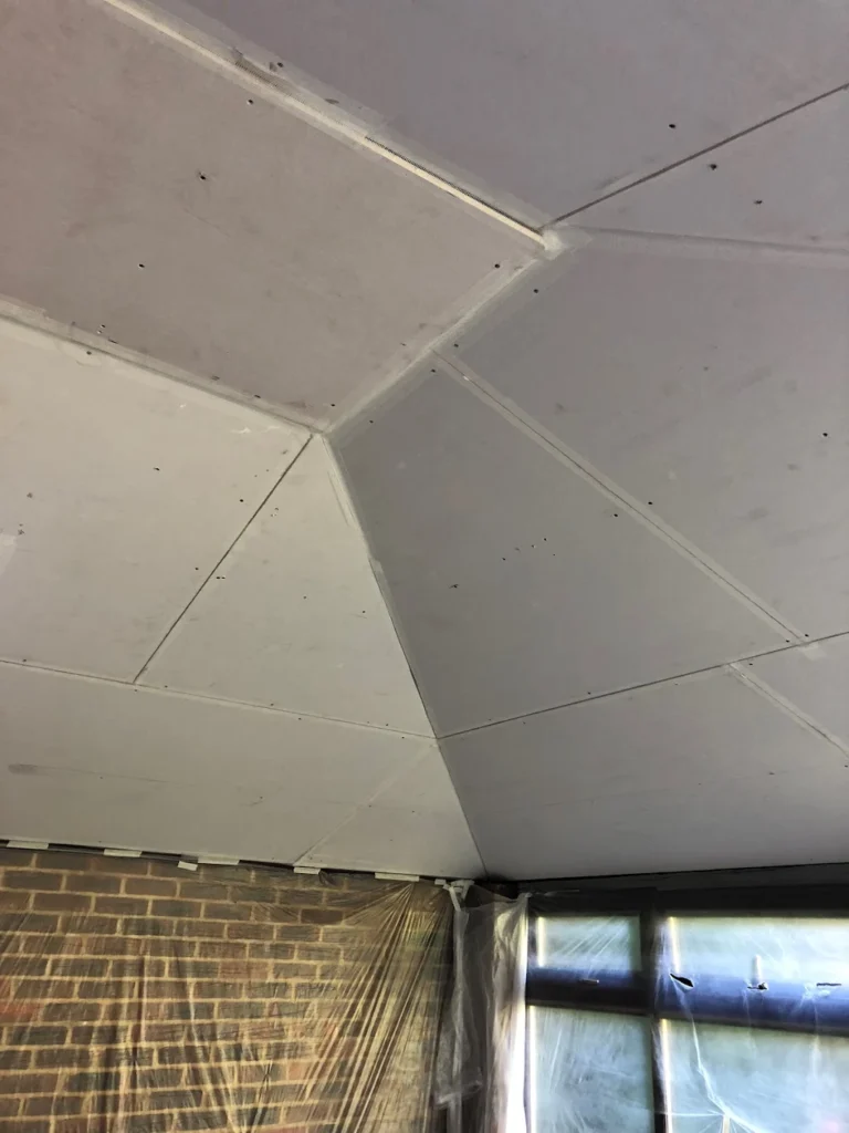 Plasterboard ceiling installation with taped joints and protected windows