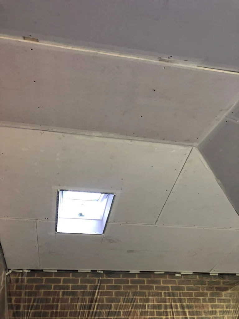 Plasterboard ceiling installation with skylight above a brick wall